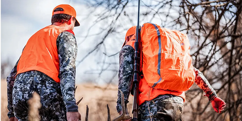 Two hunters wearing blaze orange walk through the woods.