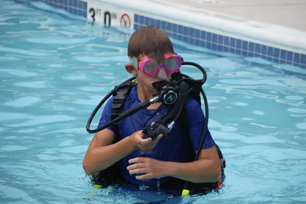 Scout wearing a pink diving mask and scuba equipment practices in a swimming pool.