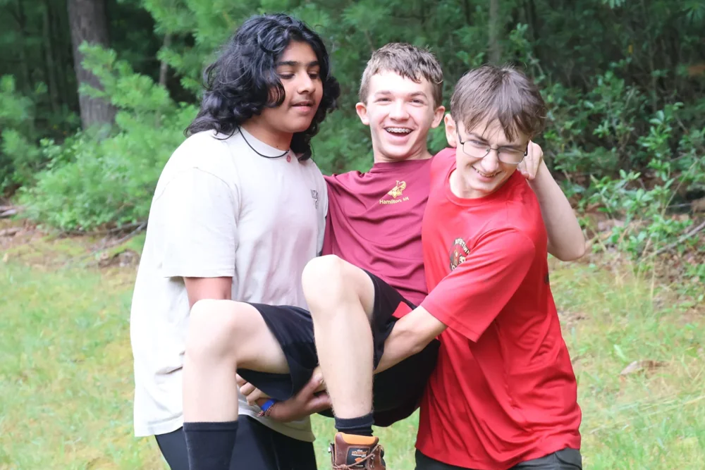 Two Scouts work together to carry a laughing friend during an outdoor skills activity.